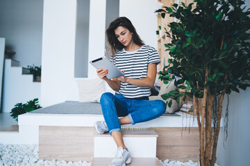 Focused young woman working online on tablet sitting on floor