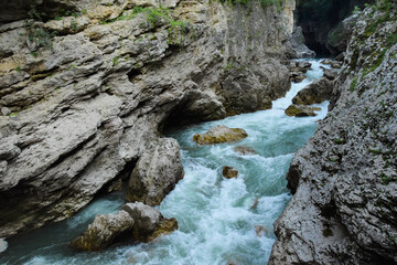 A mountain river flows among the stone rocks. The waters of the river beat against the rocks and rush into the distance in a fast stream.