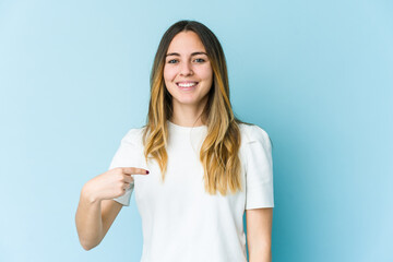 Young caucasian woman isolated on blue background person pointing by hand to a shirt copy space, proud and confident