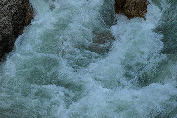 A mountain river runs among the stones. Water beats against stones and splashes fly in different directions.