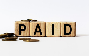 wooden cubes and PAID, coins, the concept of taxation, increase taxes and fees