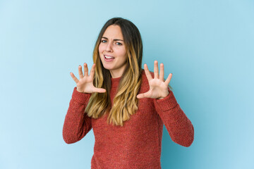 Young caucasian woman isolated on blue background upset screaming with tense hands.