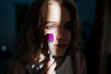 creative girl student holding a brush with pink paint near her beautiful blue eyes