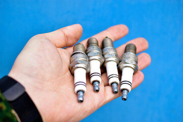 Four white car spark plugs in hand on a blue background