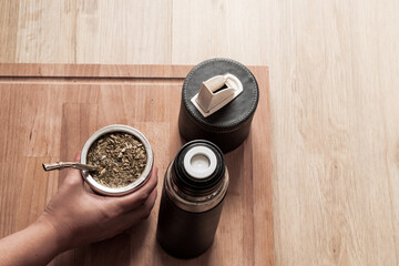 Mano sosteniendo mate, de fondo el set matero sobre fondo madera © VP Varela Pamela