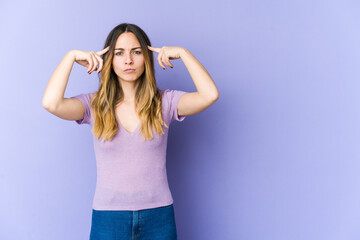 Young caucasian woman isolated on purple background focused on a task, keeping forefingers pointing head.