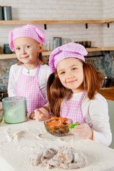 girls sit at a tabletop soiled with flour with cooked glazed gingerbread cookies