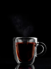 a transparent cup of tea, steam is coming from the tea, the background is dark