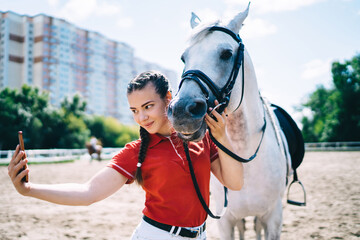 Caucasian female jockey enjoying free time for horseback in paddock country club and clicking...