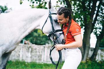 Young female equestrian stroking grey horse in countryside
