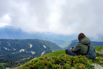 Naklejka na ściany i meble Young man sit in beautiful mountains on hiking trip. Active person resting outdoors in nature. Backpacker camping outside recreation active