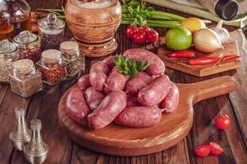 Raw brazilian sausages on the wooden board with ingredients - Linguiça toscana