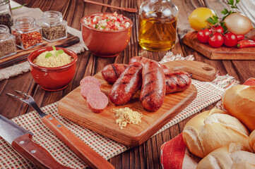 Grilled brazilian sausages on the wooden board with bread, salad, farofa and ingredients - Lingui&ccedil;a churrasco