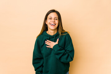 Young woman isolated on beige background laughs out loudly keeping hand on chest.