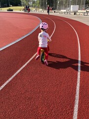 little girl riding her balance bicycle on running track in a stadium