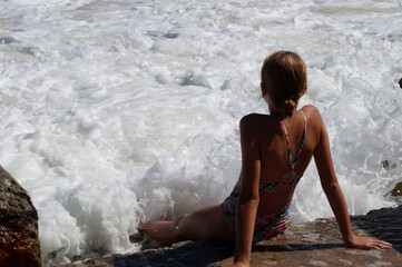 teenage girl sitting on a sandy beach in sea white foam