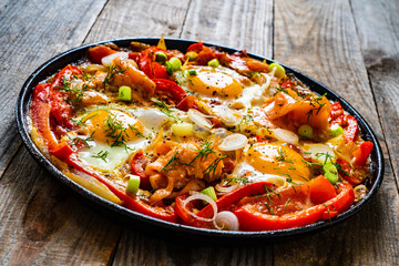 Shakshuka - fried eggs with salmon and vegetables in frying pan
