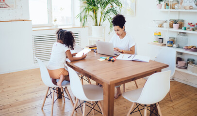 Fototapeta premium Freelance young mother using laptop sitting with little girl at home