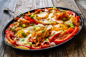Shakshuka - fried eggs with salmon and vegetables in frying pan
