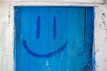 Blue wooden door with painted smile and eyes. Entrance to the house.