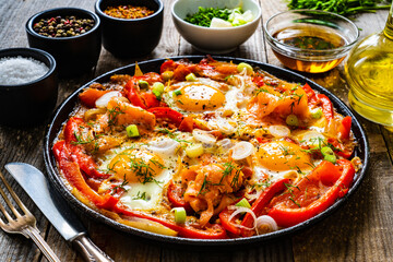 Shakshuka - fried eggs with salmon and vegetables in frying pan
