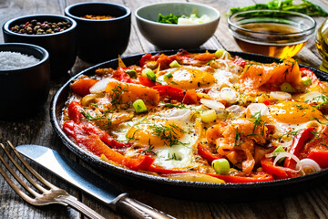 Shakshuka - fried eggs with salmon and vegetables in frying pan
