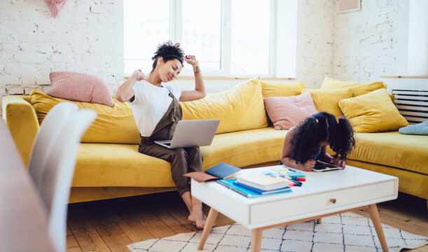Ethnic mother stretching while sitting on couch near daughter - Powered by Adobe