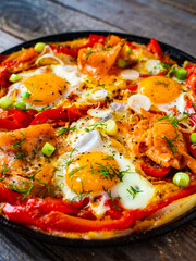 Shakshuka - fried eggs with salmon and vegetables in frying pan
