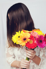 Naklejka premium Beautiful woman in white dress hid her face behind large bouquet of colorful bright gerberas.