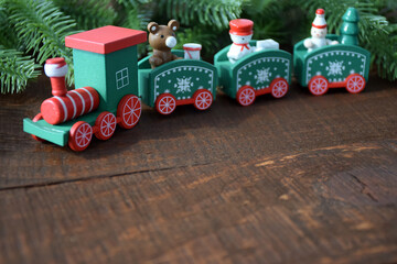 Colorful Christmas train with pine tree branches on old brown rustic pine wooden board as texture or background for design. New Year 2021, Merry Christmas frame template with copy space.