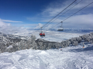 Skiers on chairlift, with view of carson valley in the background at Heavenly Ski Resort, Tahoe