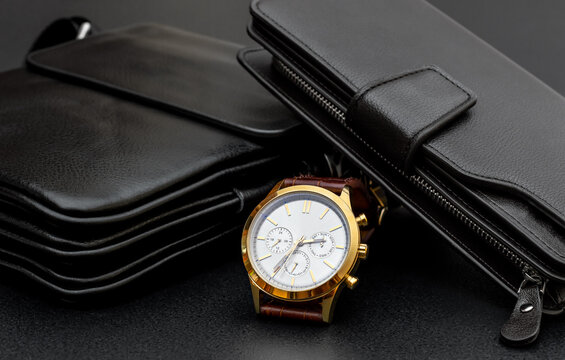 Man's wrist watch with handbag and purse on black.