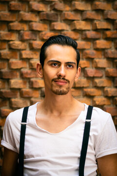 Stylish young man with a padlock beard wearing a white shirt with brick background