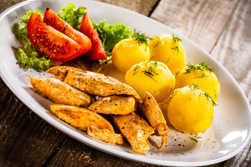 Chicken nuggets with boiled potatoes and vegetables on wooden table
