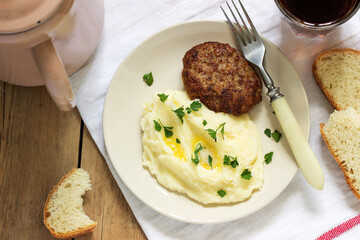Cutlet, mashed potatoes with butter and parsley and tea on a wooden table.