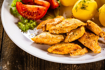 Chicken nuggets with boiled potatoes and vegetables on wooden table
