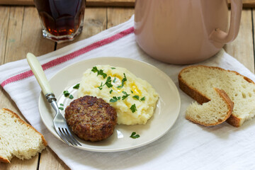 Cutlet, mashed potatoes with butter and parsley and tea on a wooden table.