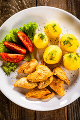 Chicken nuggets with boiled potatoes and vegetables on wooden table
