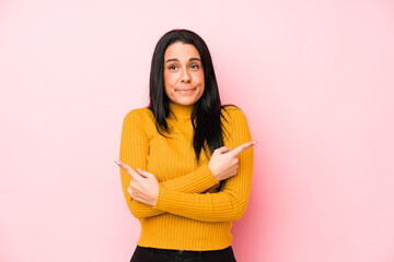 Young caucasian woman isolated on a pink background points sideways, is trying to choose between two options.