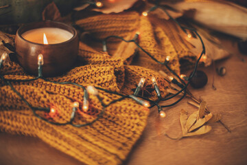 Autumn leaves, spices and candle on cozy knitted sweater in warm yellow lights. Happy Thanksgiving...