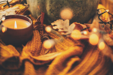 Happy Thanksgiving and Hello Fall, celebrating autumn holidays at cozy home. Autumn leaves, spices and candle on cozy knitted sweater in warm yellow lights. Selective focus