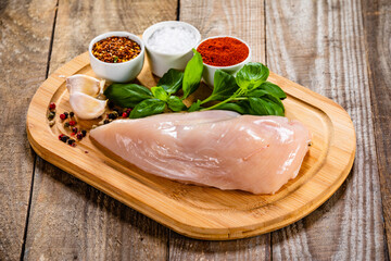 Fresh raw chicken fillet on wooden cutting board on wooden table