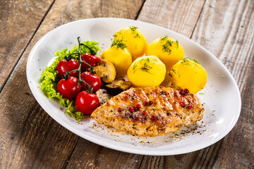 Fried chicken breast with boiled potatoes and fresh vegetables on wooden table