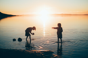 Two children playing in a lake at sunset