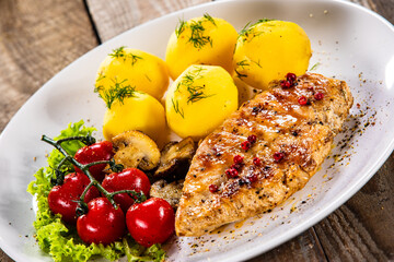 Fried chicken breast with boiled potatoes and fresh vegetables on wooden table