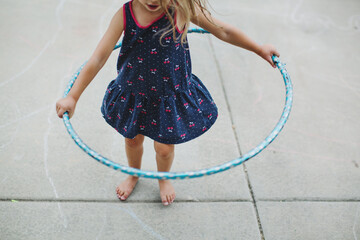 Child playing with a hula hoop barefoot on the cement
