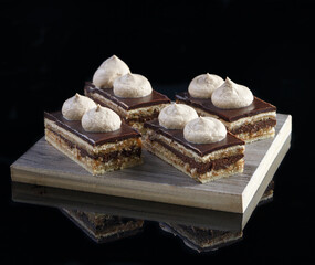 Delicious homemade sliced Opera cake with coffee on wooden stand on black reflective background