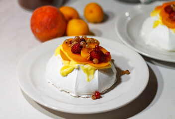 Delicious homemade Pavlova dessert with raspberries, strawberries, apricots and red currants on a white plate