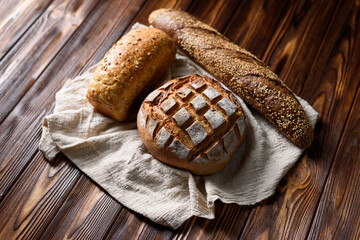 Various types of freshly baked bread on a wooden background. French baguette, white and whole grain bread on a cloth napkin. The concept of healthy bakery products.