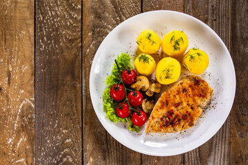 Fried chicken breast with boiled potatoes and fresh vegetables on wooden table